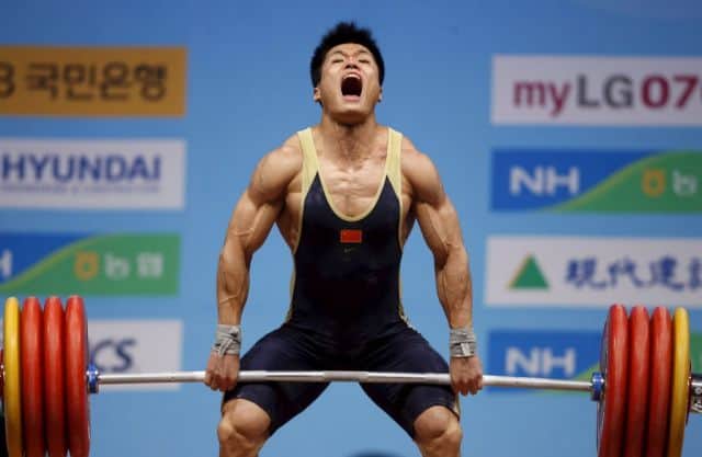 Atleta de halterofilia realizando un levantamiento en una competición, con expresión de esfuerzo poniendo a prueba el entrenamiento con periodización ondulada diaria